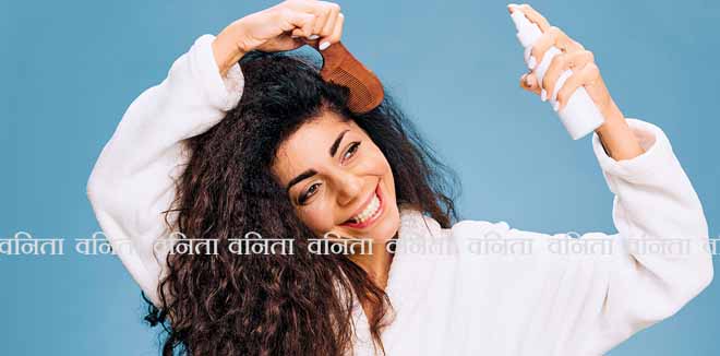2199973071 Hairstyling. Smiling tanned curly Latin lady in bathrobe Spraying On Hair For Repair split ends posing isolated on pastel blue background, using hairbrush, looking aside. Hair Care Ad Concept offer