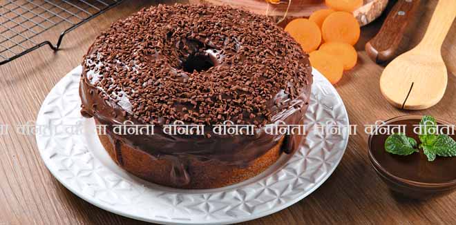 Brazilian carrot cake with chocolate frosting on wooden table with carrots in the background.