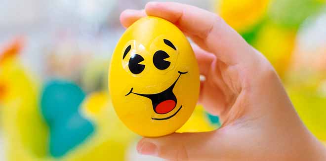 colorful chicken eggs with funny face stickers in yellow basket