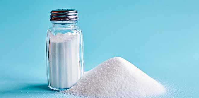 Spilled salt and saltshaker on blue background